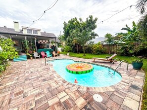 A backyard with a swimming pool, a wooden deck, and a house in the background. - NEW HOT DEAL-Charming Beachside House w. Private Pool, Walk to Beach-Flagler Ave (New Smyrna Beach)