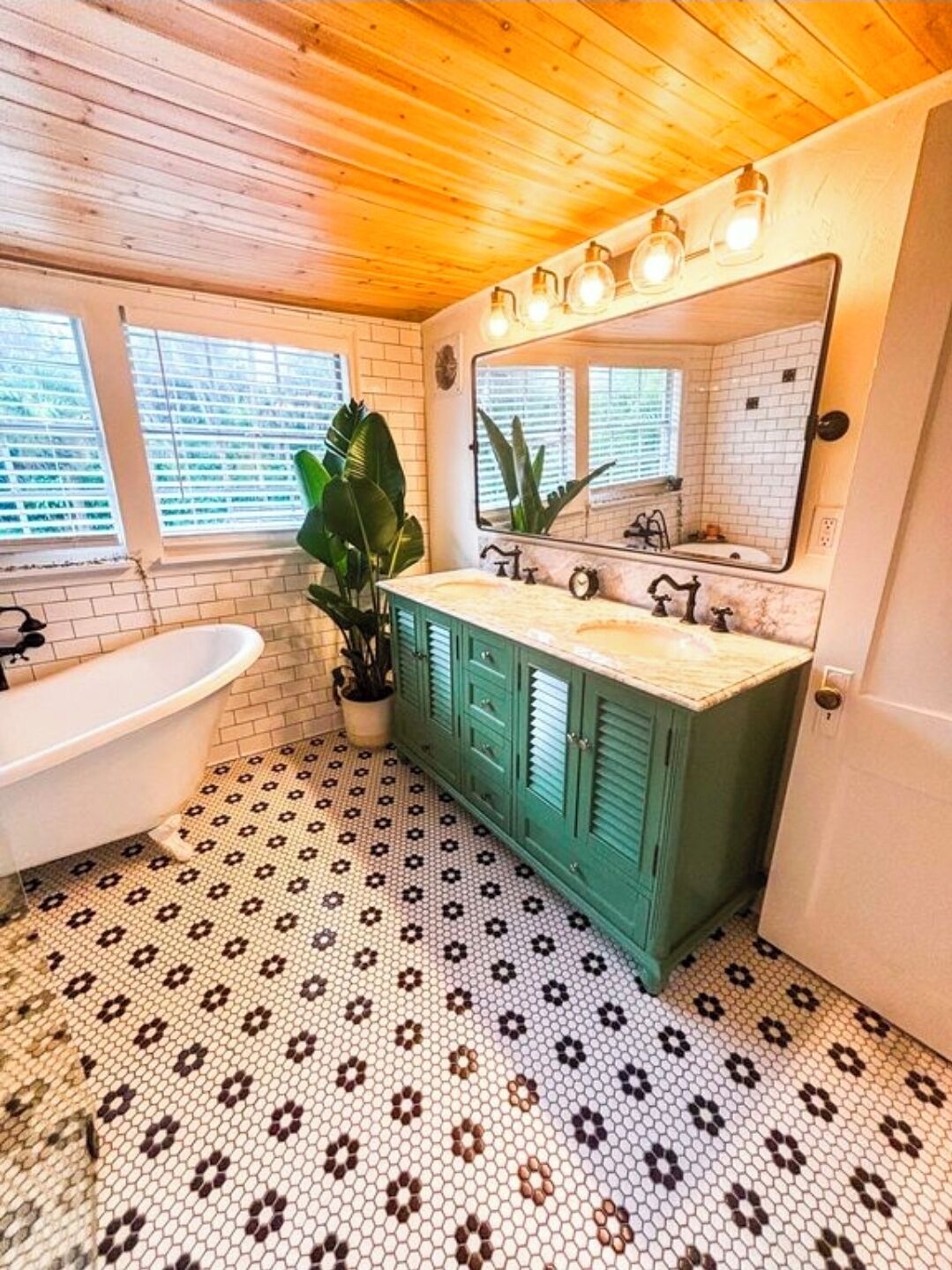 A bathroom with a white bathtub, green cabinets, a large mirror, and a patterned floor.