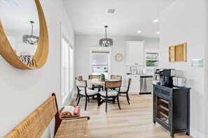 A dining area with a round table, chairs, and a bench. There is a kitchen in the background with white cabinets and a black countertop. - Salty Sunrise - Private Heated Pool Paradise In IRB Only Minutes To The Beach w/ Golf Cart (Indian Rocks Beach)
