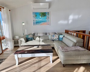 A living room with a sofa, a coffee table, and a painting of a beach scene. - Wallawa Water Views Family Retreat in Nelson Bay (Nelson Bay)