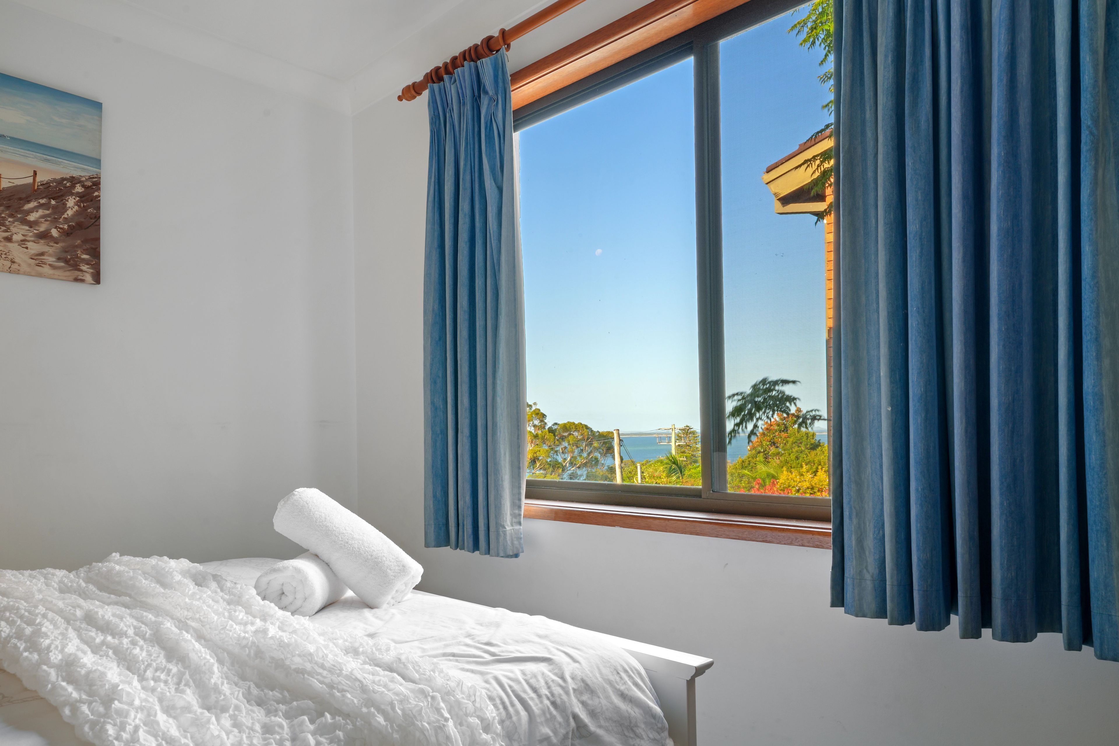 A bedroom with a bed, a window with curtains, and a painting on the wall.