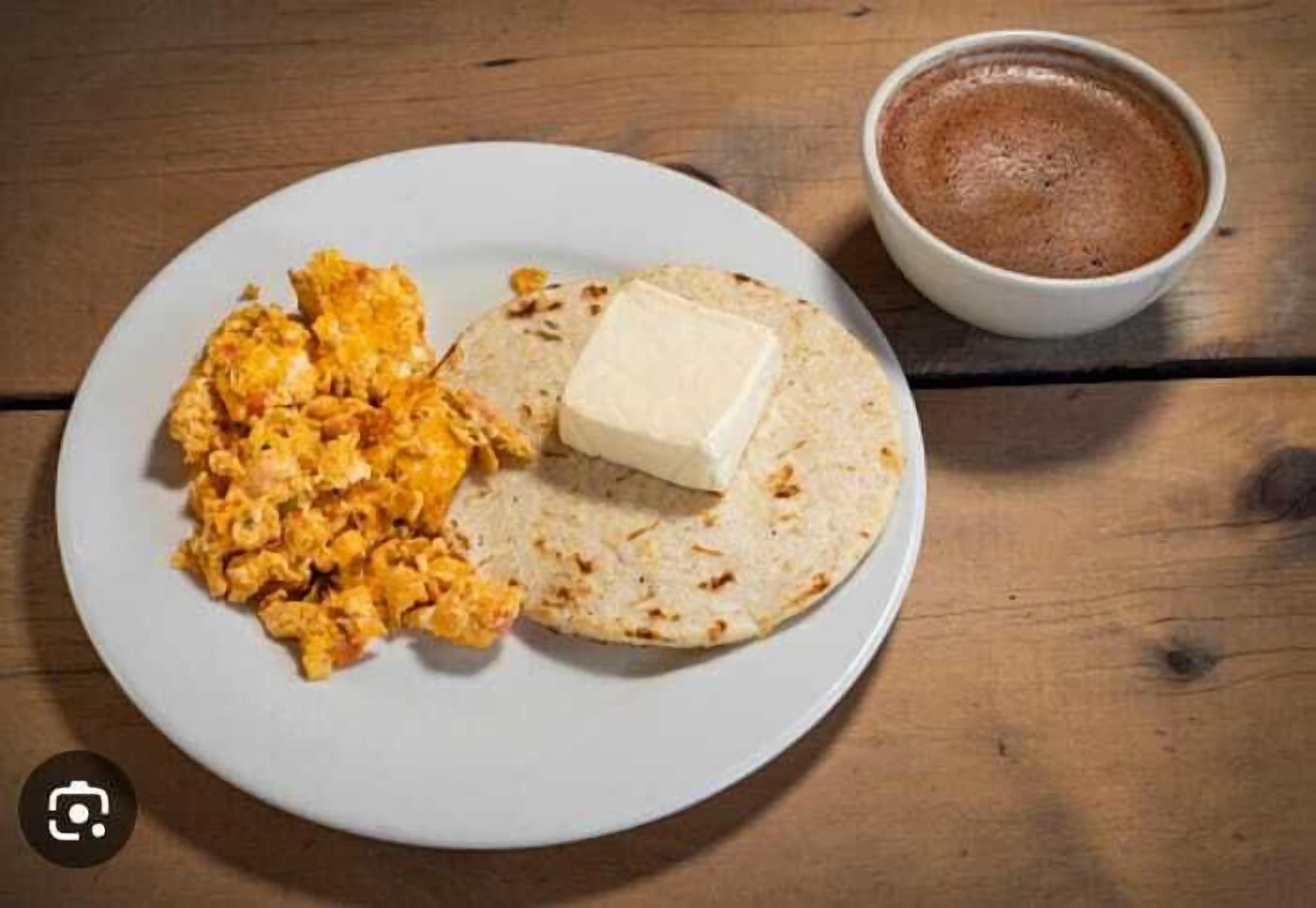 A plate with scrambled eggs, a piece of buttered toast, and a cup of coffee on a wooden table.