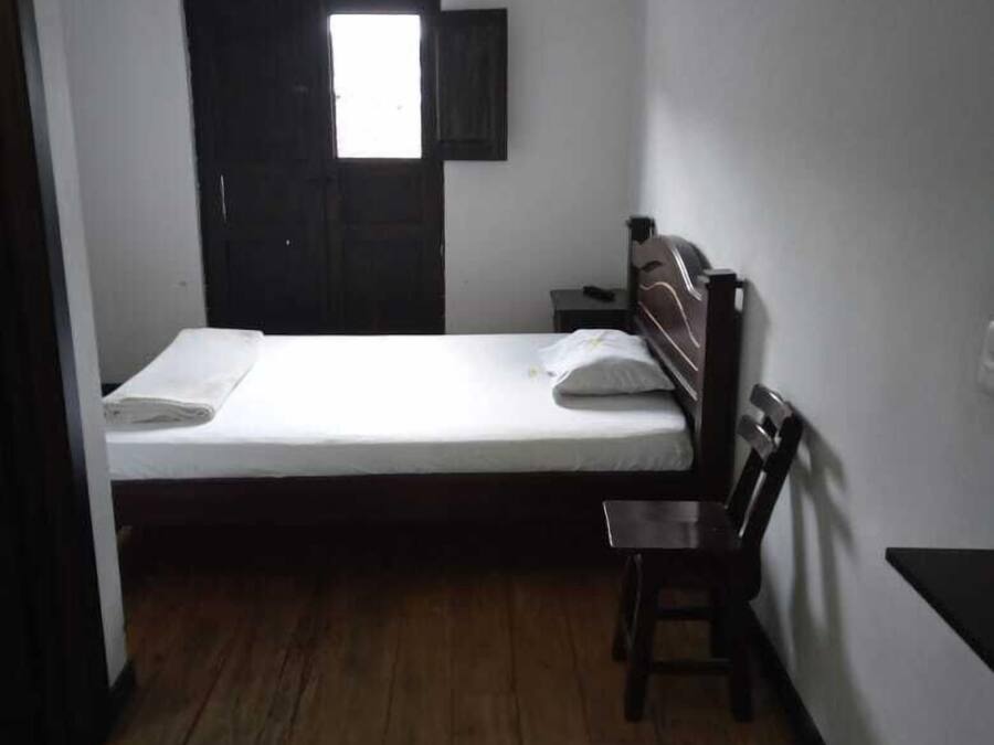 A small, single-bed room with a wooden floor, a desk, and a chair.