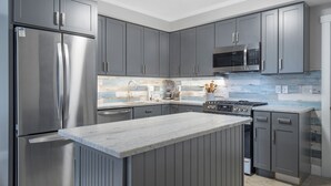 A modern kitchen with grey cabinets, stainless steel appliances, and a marble countertop. - Oceanfront 2-bedroom Condo with Private Beach! (Dennis)