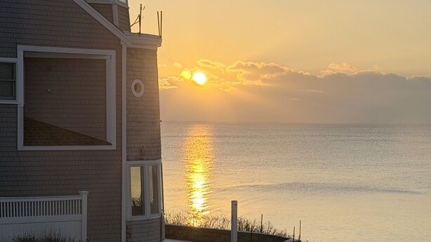 A coastal building with a balcony overlooking the sea, a clear view of the sunset, and a snow-covered ground. - Oceanfront 2-bedroom Condo with Private Beach! (Dennis)