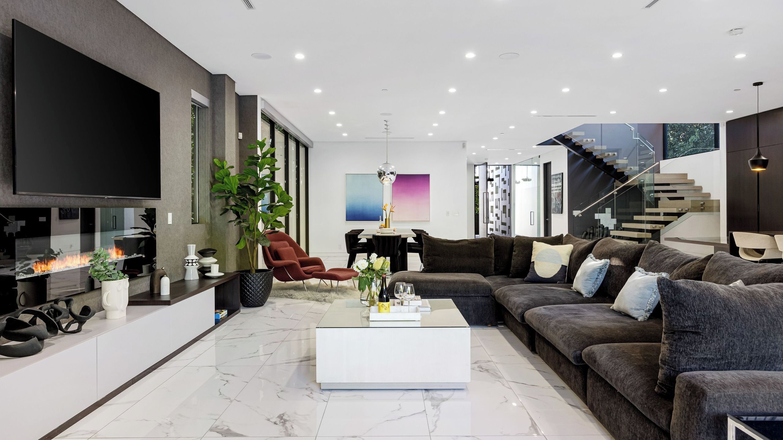 A modern living room with a large flat-screen TV, a fireplace, a sofa, and a staircase.