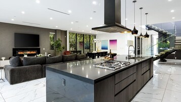 Una cocina moderna con una isla grande, una zona de comedor con mesa de vidrio y una sala de estar con sofá amplio y televisor de pantalla plana.
