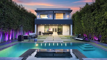Una casa moderna de dos pisos con piscina, mobiliario exterior y un jardín bien cuidado.
