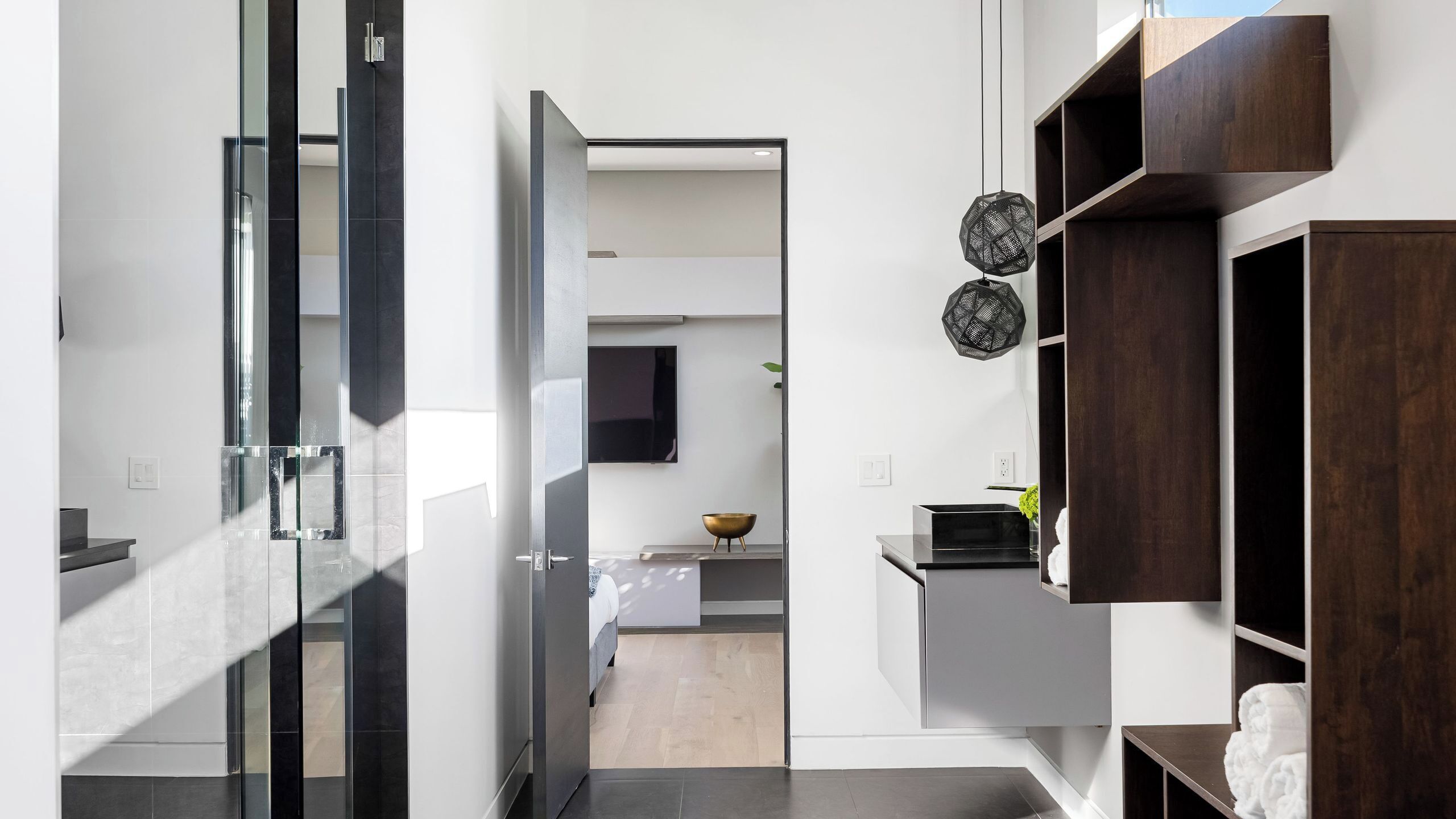 Un intérieur moderne avec une porte vitrée donnant sur la cuisine, un téléviseur à écran plat fixé au mur et une étagère en bois.