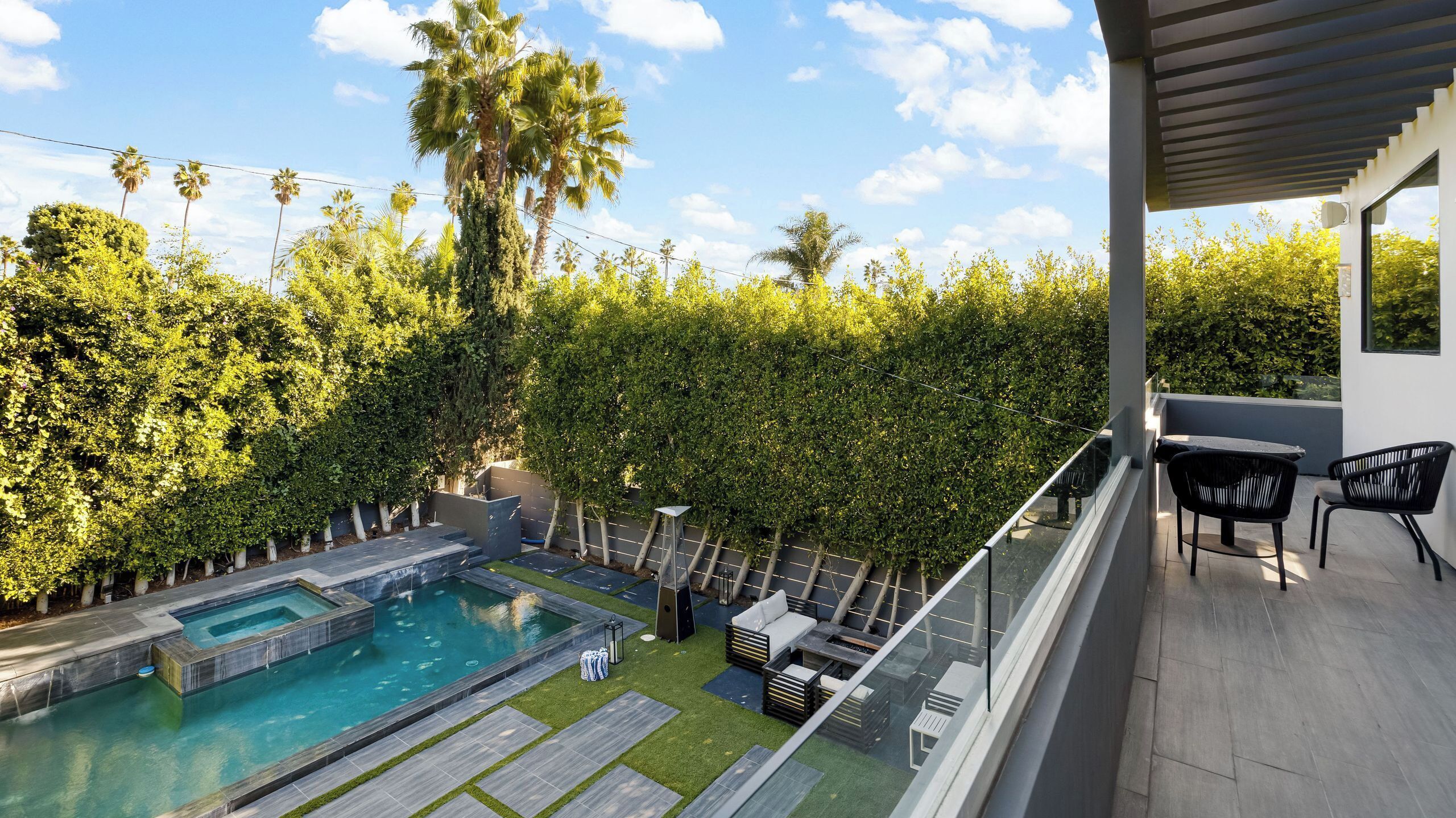 A rooftop pool with a view of a lush garden and a balcony with outdoor furniture.