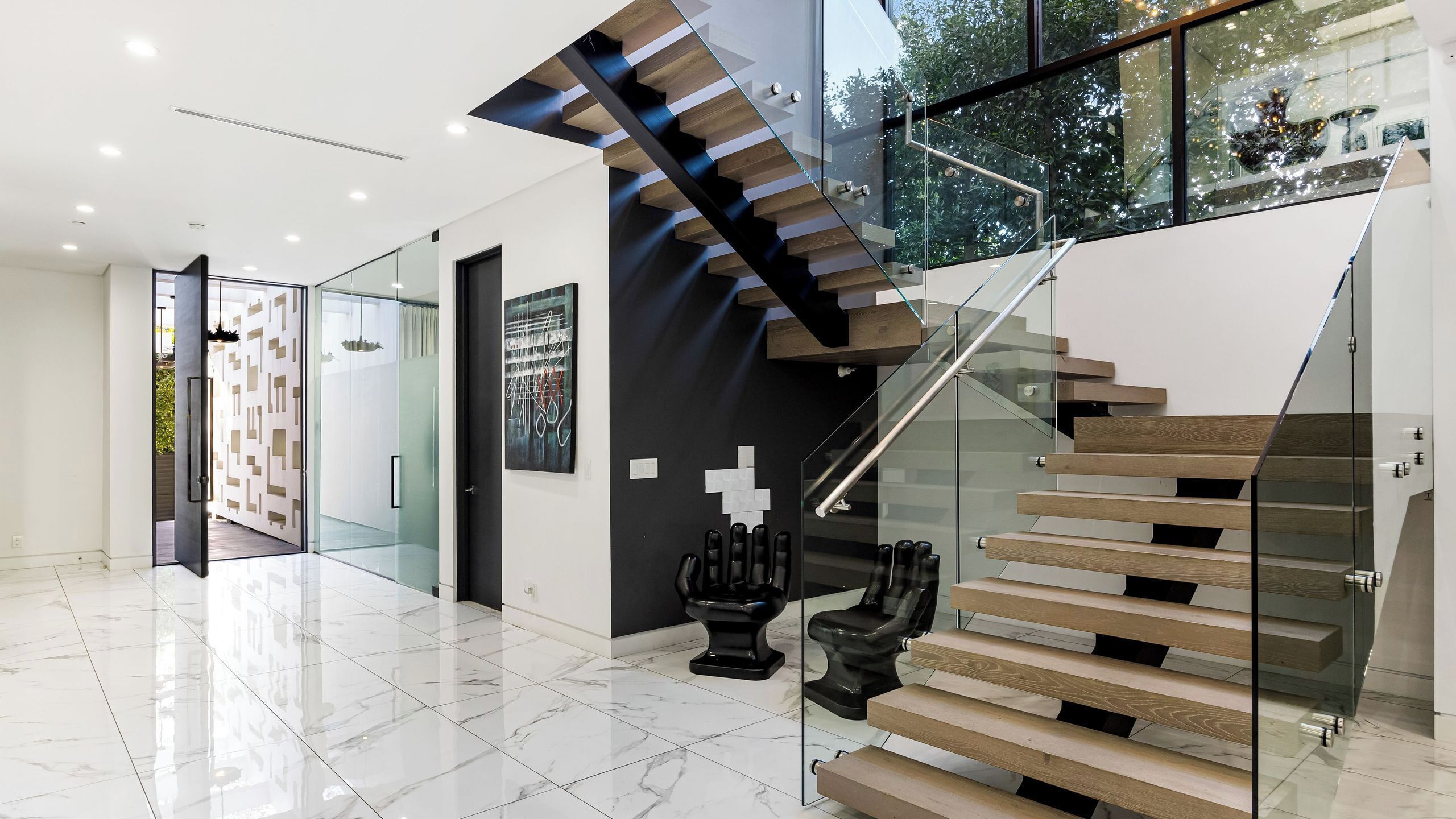 A modern interior with a glass staircase, a marble floor, and contemporary art pieces.