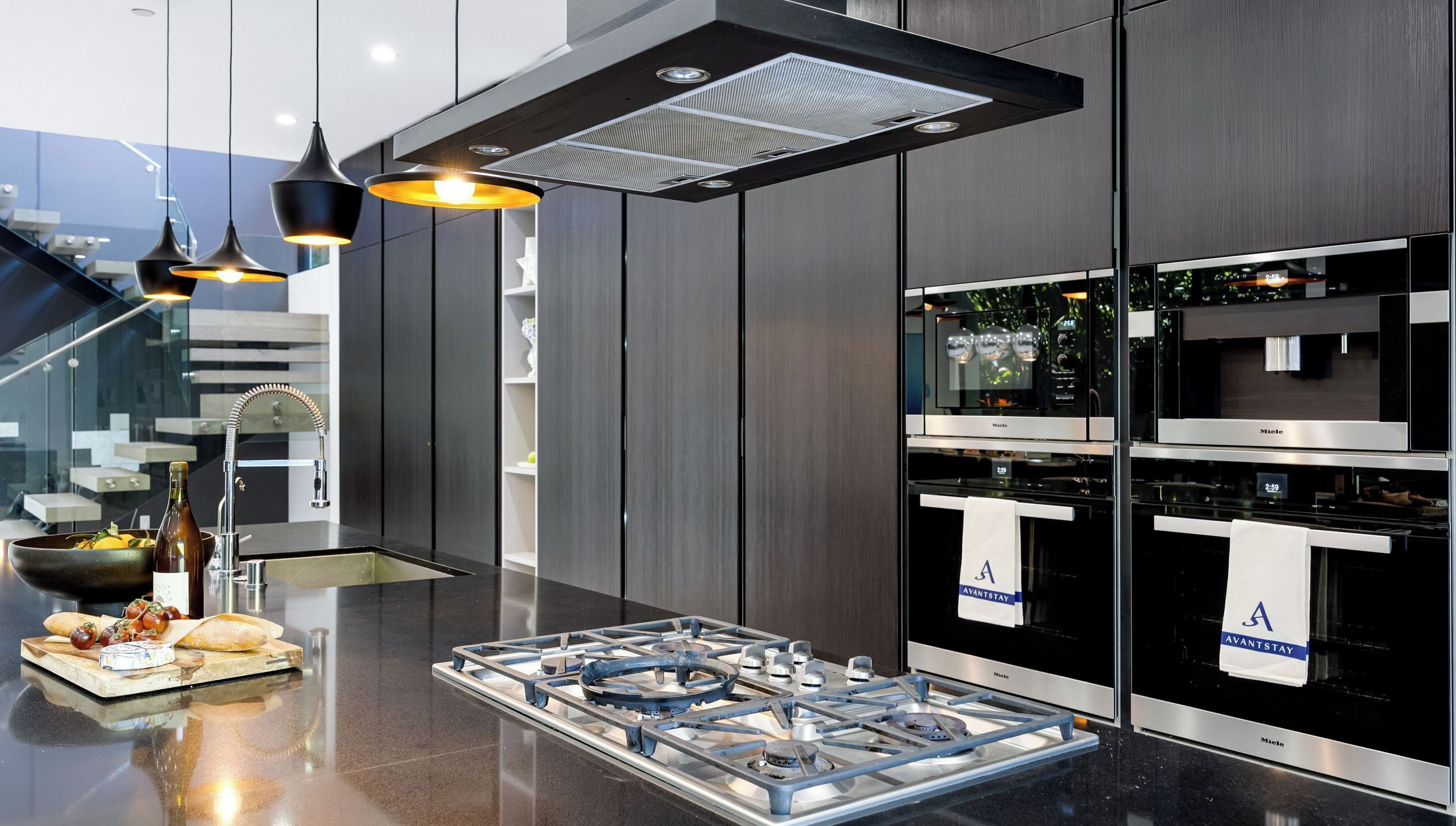 Une cuisine moderne dotée d’une cuisinière à gaz, d’appareils électroménagers en acier inoxydable, d’un éclairage suspendu et offrant une vue sur la ville.