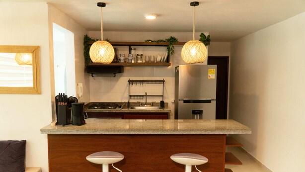 Une cuisine moderne dotée d’un îlot central, de tabourets de bar, de luminaires suspendus et d’un réfrigérateur en acier inoxydable.