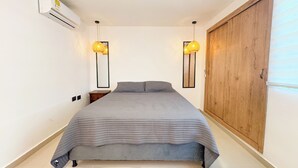 Une chambre à coucher comprenant un lit, deux lampes fixées au mur, une armoire en bois et un appareil de climatisation.