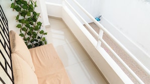 Un balcon avec un canapé beige, une balustrade blanche et un pot de fleurs.