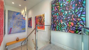 Um corredor com arte abstrata, uma escada e um vaso em uma estante.