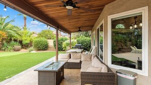 A covered patio area with a seating arrangement, a glass-top table, and a ceiling fan.