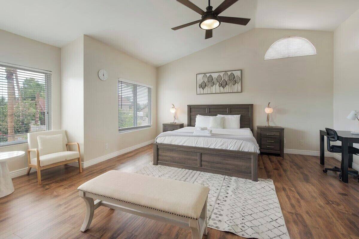 A bedroom with a bed, bedside tables, a chair, a desk, and a ceiling fan.