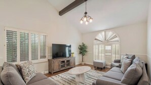 A living room with a large TV, two sofas, a coffee table, and a chandelier.