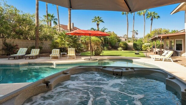 A hot tub with a surrounding pool area, lounge chairs, and a red umbrella.