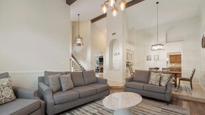 A spacious living room with two grey sofas, a round coffee table, and a striped rug. A staircase leads to an upper level.