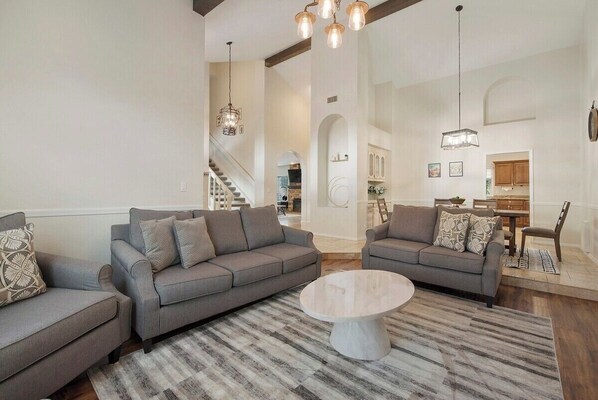 A spacious living room with two grey sofas, a round coffee table, and a striped rug. A staircase leads to an upper level. - Scottsdale Retreat - Heated Pool (Scottsdale)