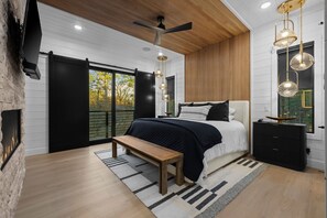 A modern bedroom with a bed, bench, and a TV mounted on the wall. - Luxury Cabin w/ Golf Sim & Pickleball Court (Broken Bow)