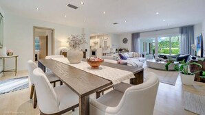 A modern living room with a dining area, a kitchen, and a large window offering a view of the outdoors. - High-End House with Heated Pool, outdoor TV (Miami Shores)