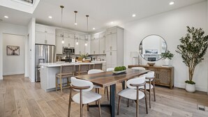 Eine moderne Küche mit weißen Schränken, Edelstahlgeräten und einem Holzespeisetisch mit weißen Stühlen.