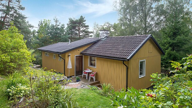 A small wooden cabin with a sloped roof, a front porch with a table and chairs, and a garden area. - Lovely home in Ljungskile with WiFi (Ljungskile)