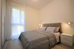 A bedroom with a bed, a nightstand, and a window with curtains. - Holiday apartment with air conditioning and balcony (Bibione)