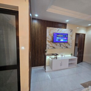 A modern living room with a flat-screen TV mounted on a marble wall, a white entertainment unit with integrated lighting, and a wooden panel accent. - STUDIO HAPPY HOME (Dakar)