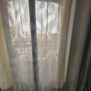 Ein Fenster mit einem durchscheinenden Vorhang, der einen Blick auf ein Mehrstöckiger Gebäude mit Balkonen freigibt.