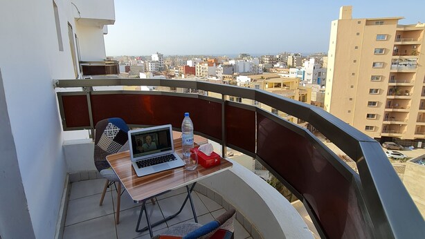 Un balcon avec une table, des chaises, un ordinateur portable et une bouteille d’eau.