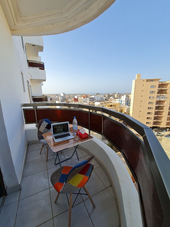 A balcony with a table, chairs, a laptop, and a bottle of water. - STUDIO HAPPY HOME (Dakar)