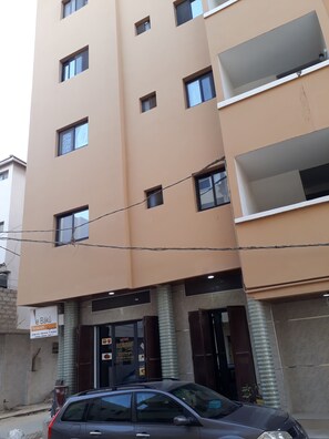 A multi-story building with a beige facade, several windows, and a parked car in front. - STUDIO HAPPY HOME (Dakar)