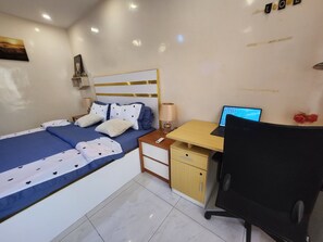 Ein Schlafzimmer mit einem Bett, einem Schreibtisch mit Laptop, einem Stuhl, einem Nachttisch und einem an der Wand befestigten Regal.