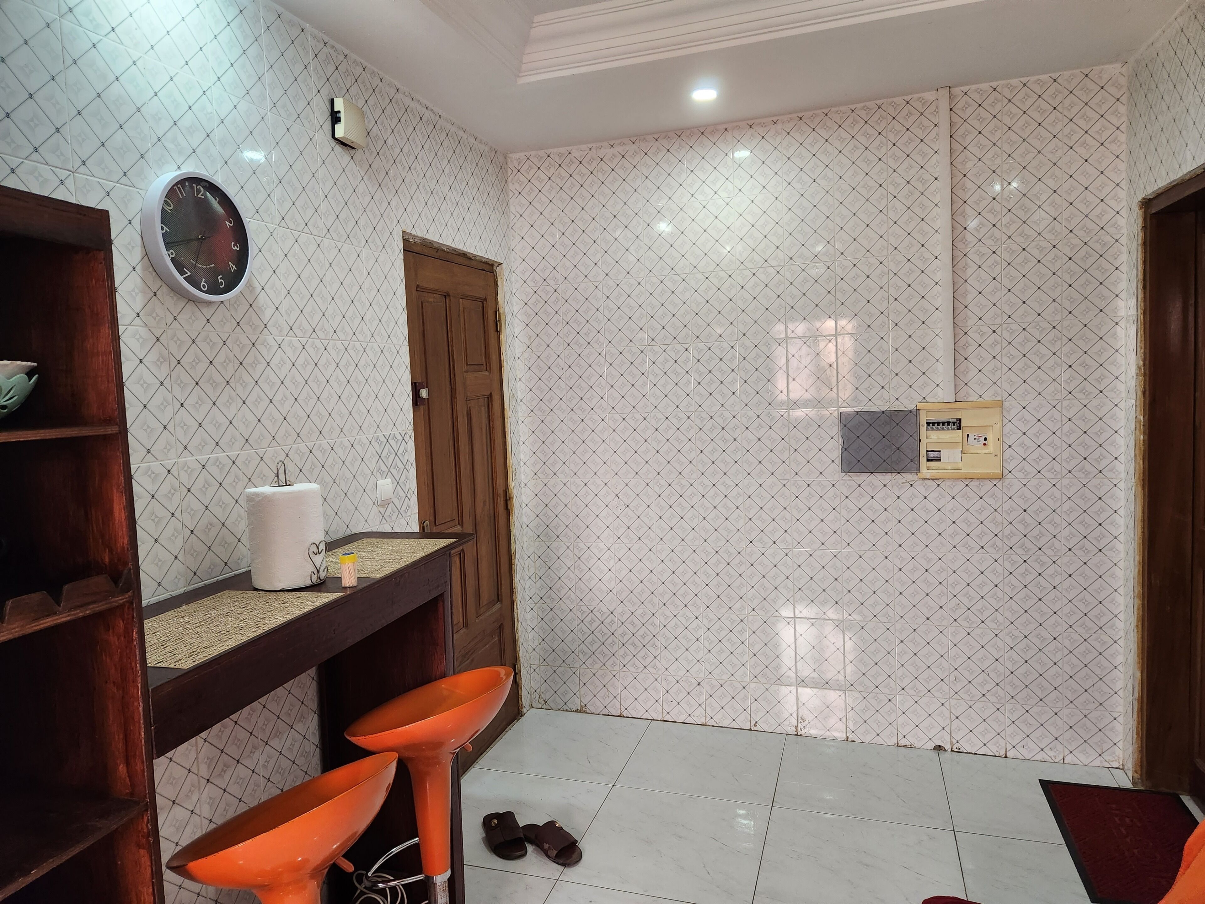 Une salle de bain avec un mur carrelé, une porte en bois, une horloge, un distributeur de serviettes et un petit panneau électrique.