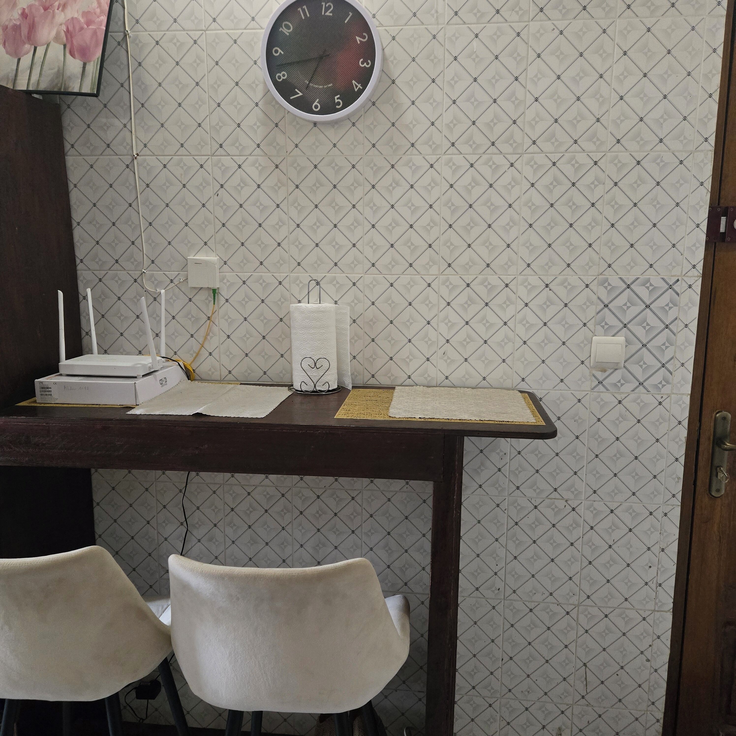 A room with a desk, two chairs, a clock, and a patterned wall.