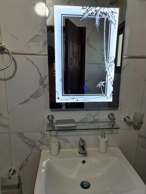 A bathroom with a marble backsplash, a glass shelf above the sink, and a mirror with a decorative frame. - STUDIO HAPPY HOME (Dakar)