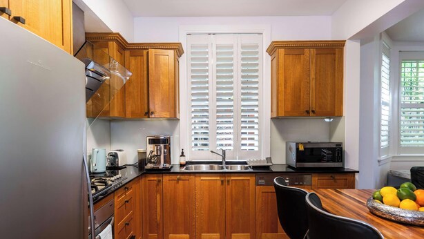 Cocina compacta con armarios de madera, una estufa de acero inoxidable, un microondas y una mesa de comedor con fruteros.