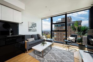 Ein modernes Wohnzimmer mit Sofa, Couchtisch und Blick auf die Stadt durch große Fenster.