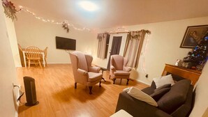 Un salon avec un plancher en bois, deux fauteuils, un canapé, une petite table blanche, un téléviseur fixé au mur et un sapin de Noël.