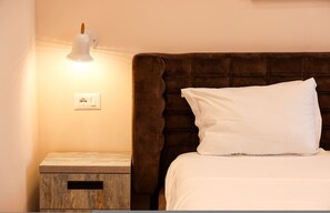 A neatly made bed with a white pillow and a brown headboard. There is a bedside table with a lamp and a power outlet. - Grandstay Apartments 011 (Durrës)