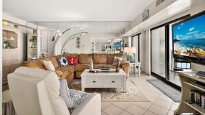 A modern living room with a sectional sofa, a white coffee table, and a television on a stand. - 2 BR Condo w/ Sunrise and Sunset Views (Ocean City)