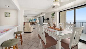 A spacious dining area with a glass table, white chairs, and a ceiling fan. - 2 BR Condo w/ Sunrise and Sunset Views (Ocean City)