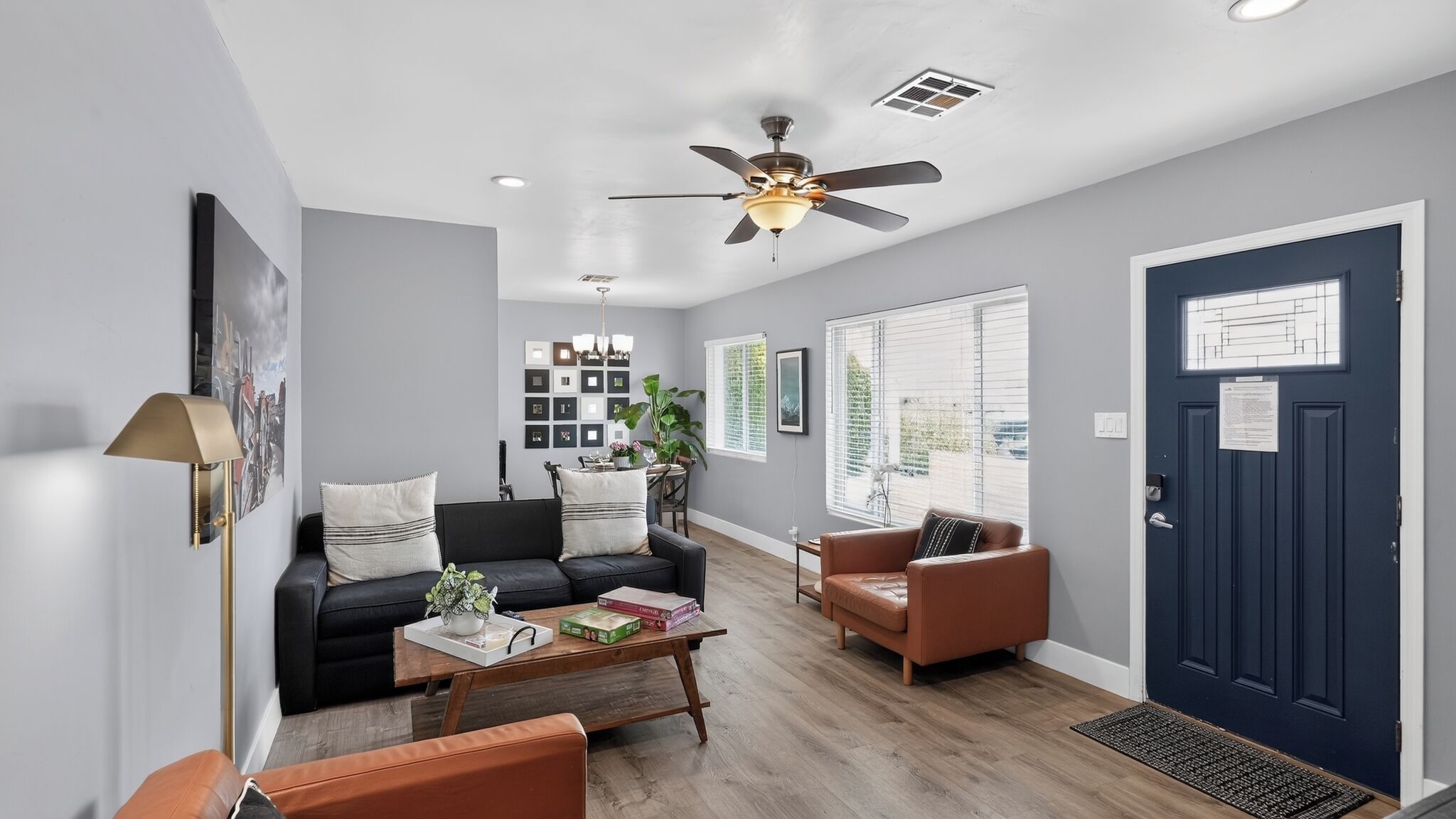 A modern living room with a ceiling fan, a dark blue door, and a dining area with a table and chairs.
