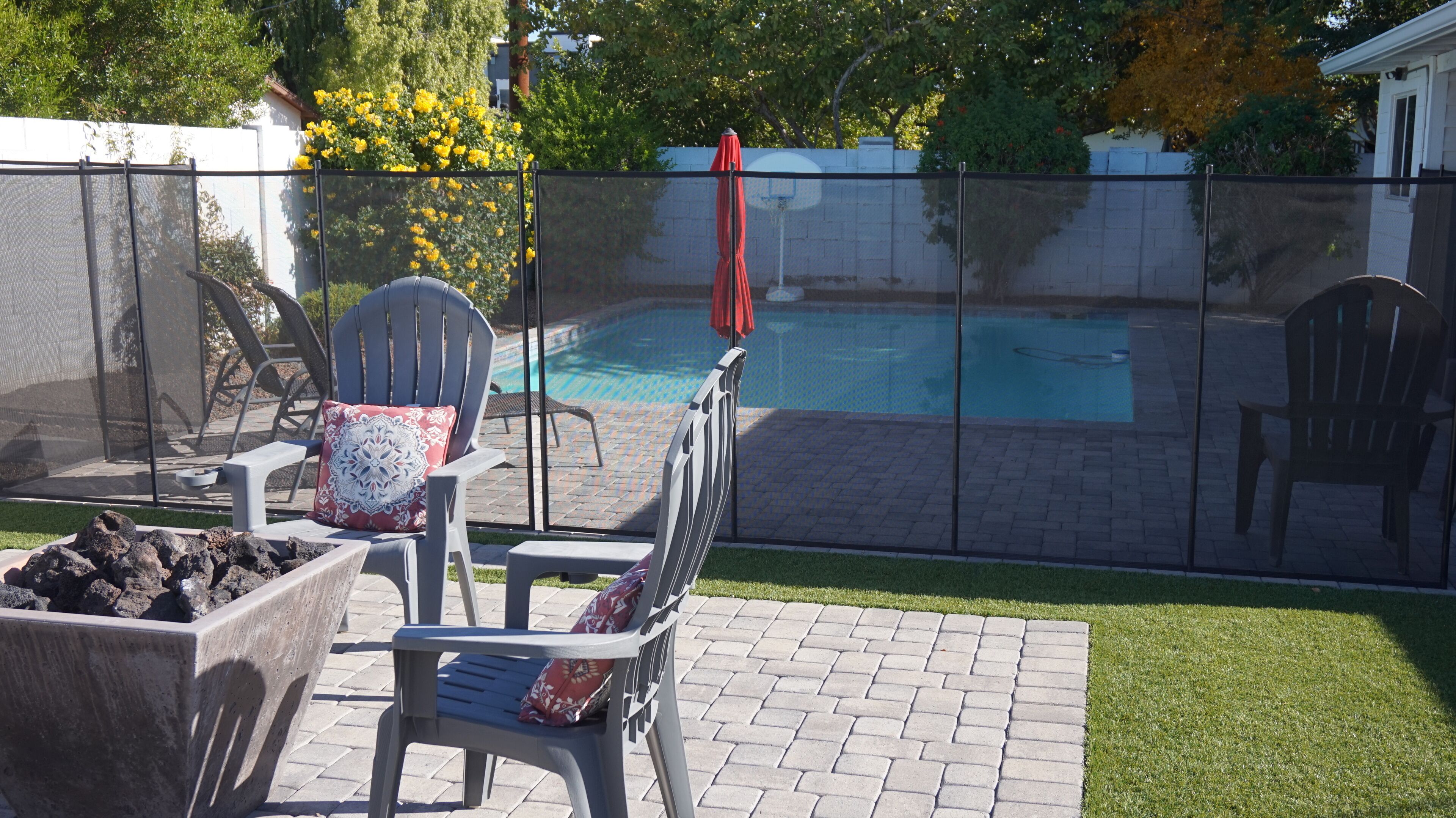 A backyard with a pool, patio chairs, and a red umbrella.