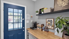 A room with a blue door, a coffee machine, a shelf with books and a plant, and a framed picture of a coffee shop. - Walk to Old Town - Scottsdale Home with Pool (Scottsdale)