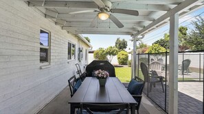 Een overdekt terras met een tafel, stoelen, een plafondventilator en een barbecue.